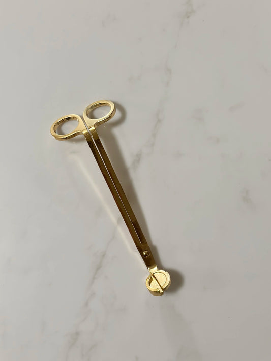 Gold-colored tool with a heart-shaped end on a light gray marble background